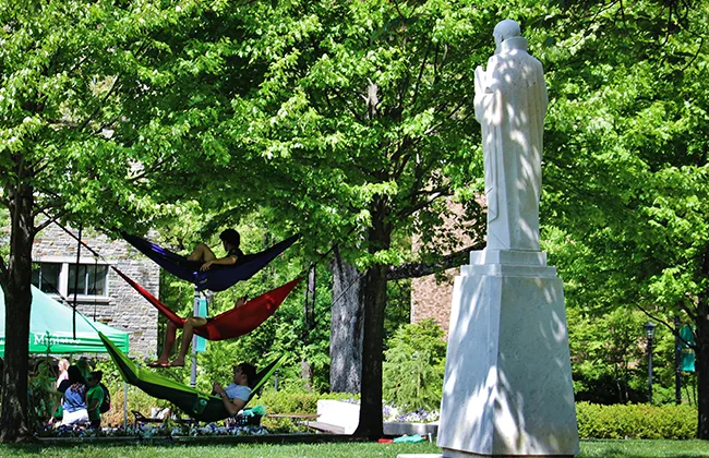 Students lounging in hammock near the Loyola Ignatius statue