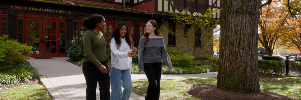 Three students walk and chat in front of Humanities Center.