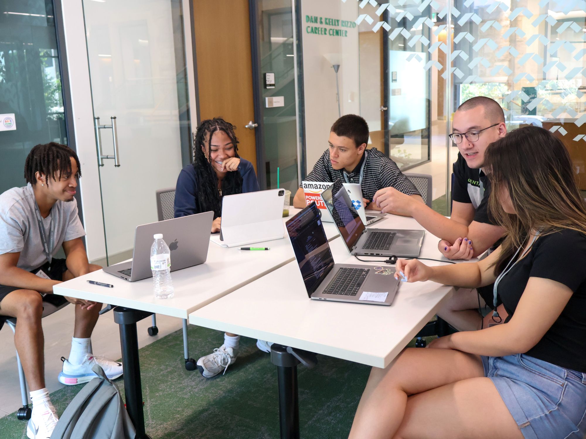Students sitting at tables work together on laptops.