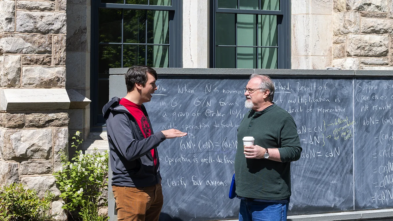 A student and professor talking outside in front of a chalkboard - Press enter to play