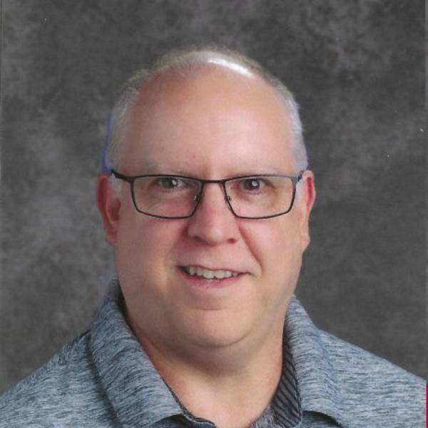Headshot of Dr. Alan Thoms-Chesley in white/black heather polo on grey background