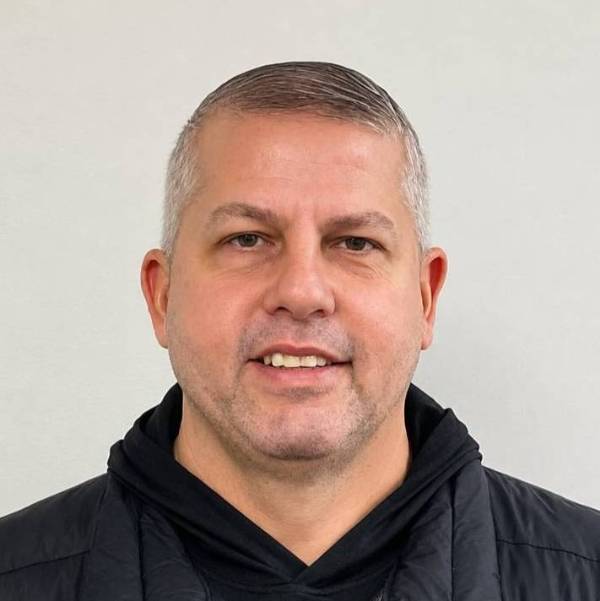 Wade Zufall headshot with black hoodie and vest on white background