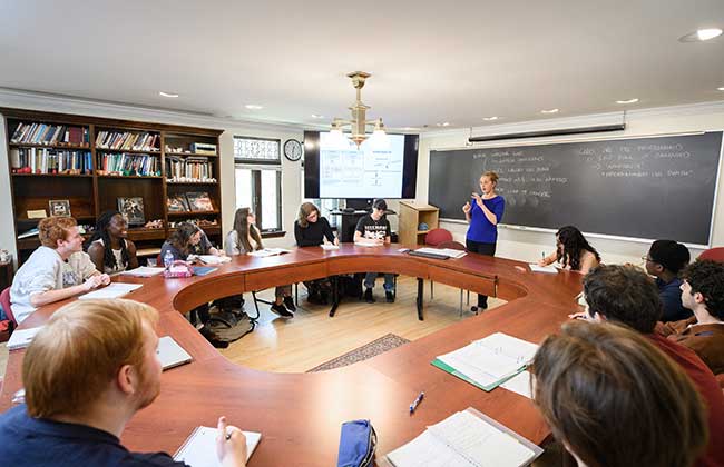 Student in a circular table setting listening to a lecture in a warm colored room