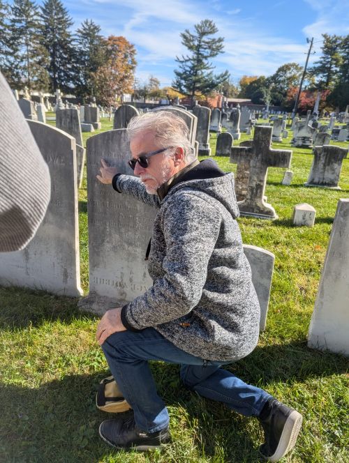 Dr Colombat on one knee explaining something on a grave stone