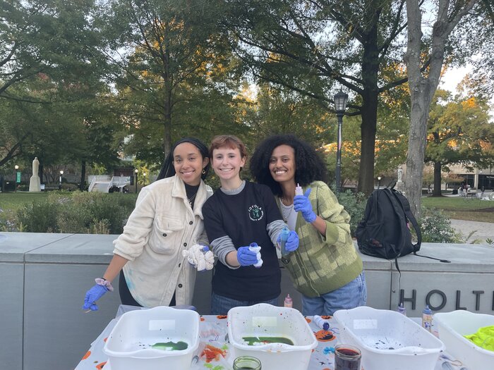 Sociology Club co-presidents Aisha, Ella, and Hanna smiling during a tie-dye event on the quad.