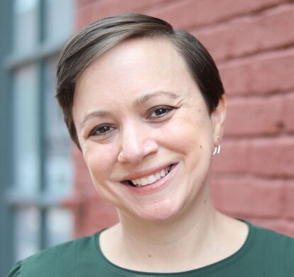 Dr. Natka Bianchini smiling while wearing a green shirt with a red brick wall in the background