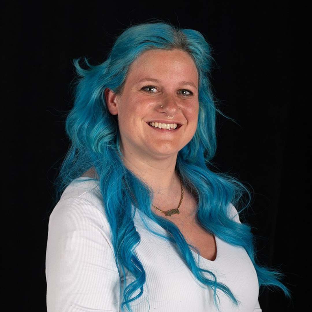 Headshot of Professor Heather Braxton with blue hair and a white shirt in front of a black background