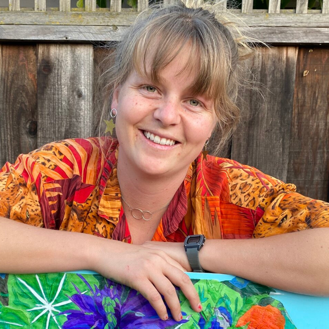 Katie Peck posing with a colorful artwork with a wooden fence in the background