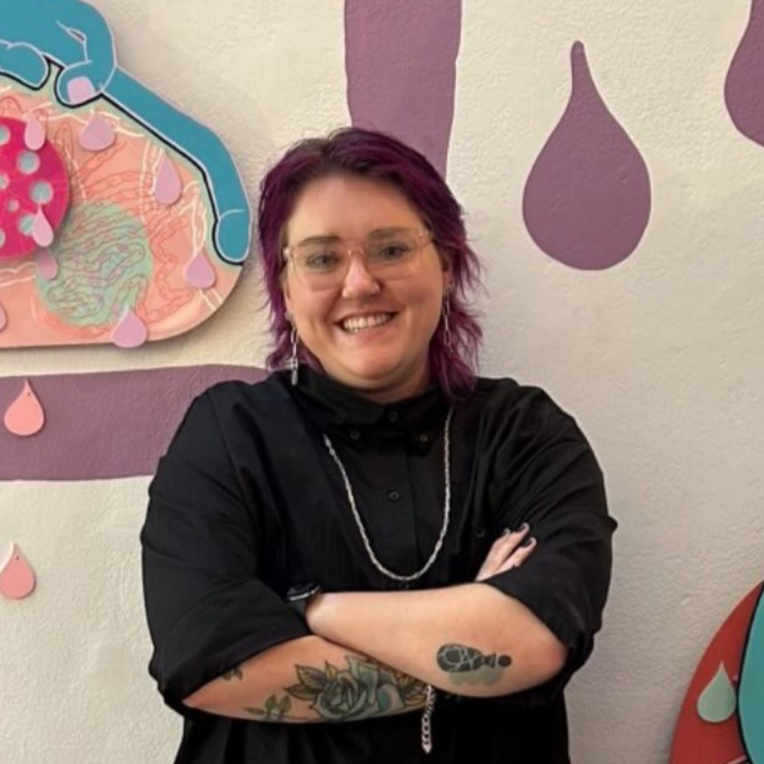 Beth Yashnyk leaning against a wall with their art
