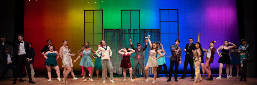 Performers in colorful costumes on a stage with a vibrant, multi-colored backdrop.