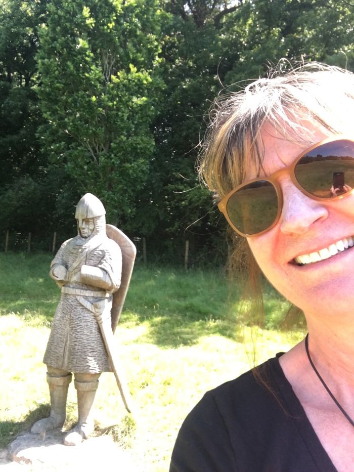 Kathy Forni with sunglasses posing with a Medieval statue
