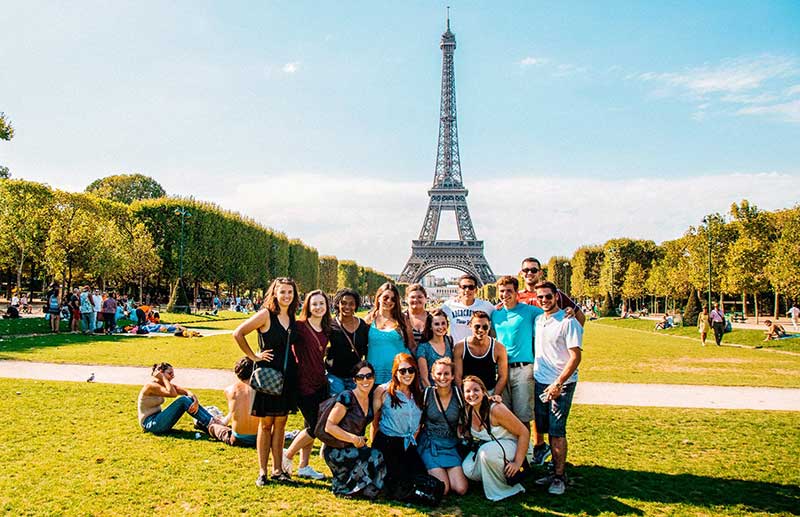 Students posing for a group photo on a bright sunny day in Paris by the Eiffel Tower