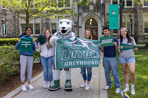 Undergraduate students and Iggy the greyhound stand with their Loyola University Maryland gear 