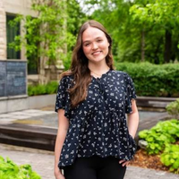 Tara Larson, ‘26, smiles with greenery in the background