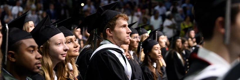 Loyola graduates in caps and gowns watching the Commencement ceremony on the stage out of frame