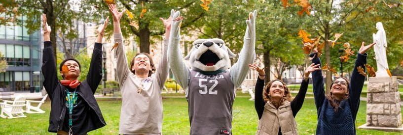 Students and Loyola's mascot Iggy on the Quad with their arms raised in the air
