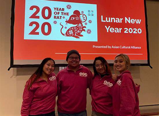 Four students posing together in front of a projector screen decorated for the 2020 Lunar New Year