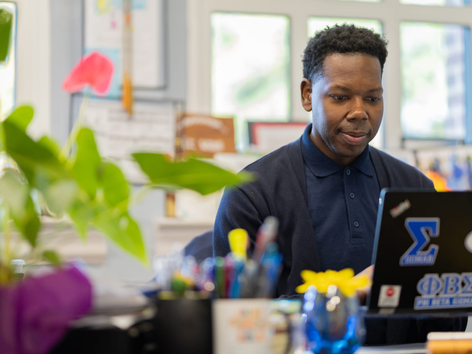 a student looking a laptop screen on a desk with a plant on it