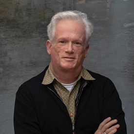 white haired man in sweater with arms crossed