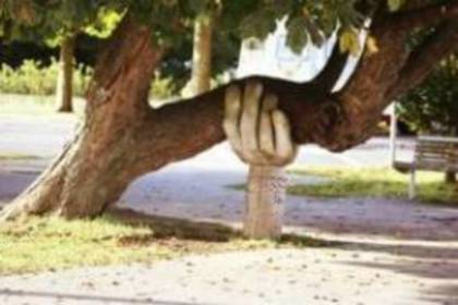 A sculpture shaped like a hand holding up a leaning tree in the park