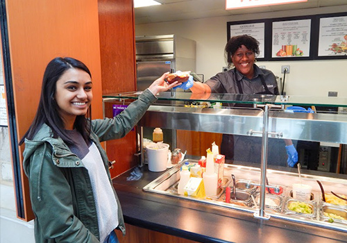 Food service employee handing food to a smiling student