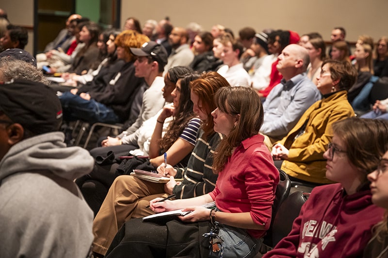 Assembled university community members gather and listen in a large meeting room