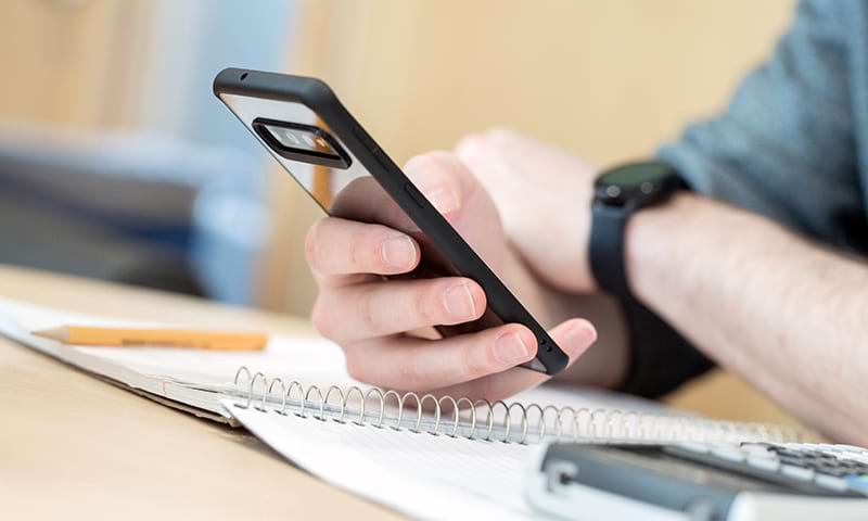 A close up of a student holding a phone over a notebook, pencil, and calculator