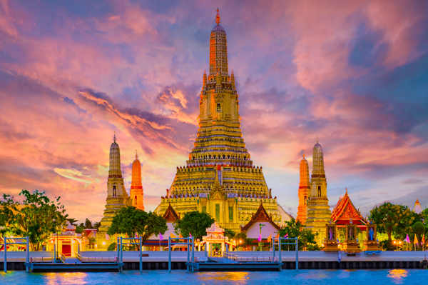 Wat Arun temple in Bangkok thailand, a tall temple with a myriad of sunset colors behind it.