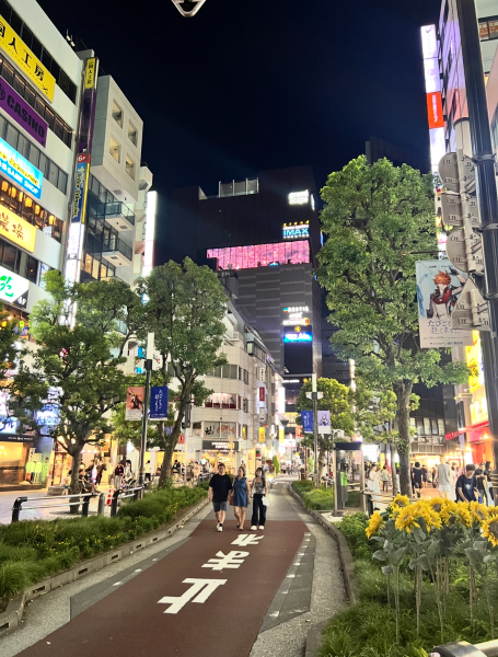 Ikebukuro Japan, trees growing in a deeply technological city with lots of colorful lights on tall buildings. People walking through the streets.