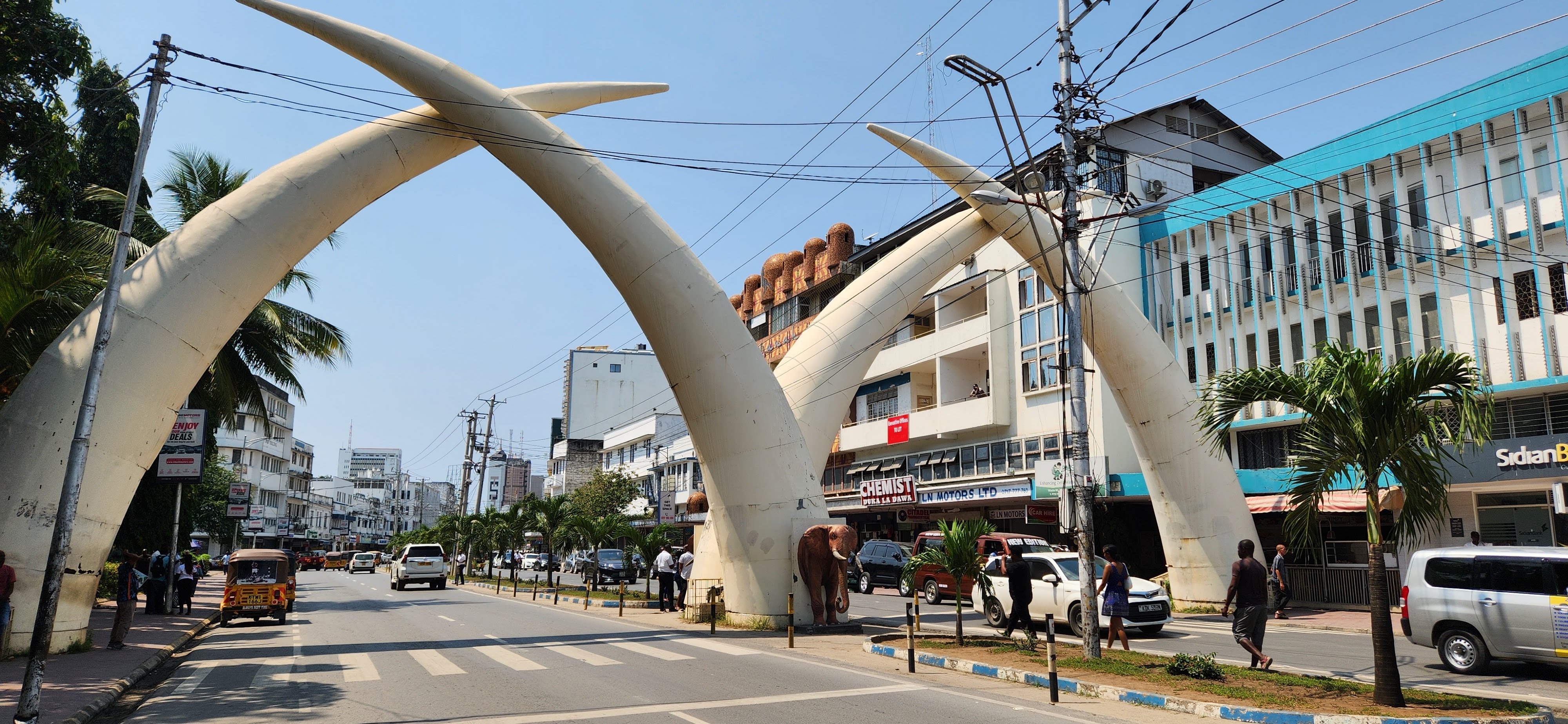 Elephant tusks creating an arch as cars enter a city.