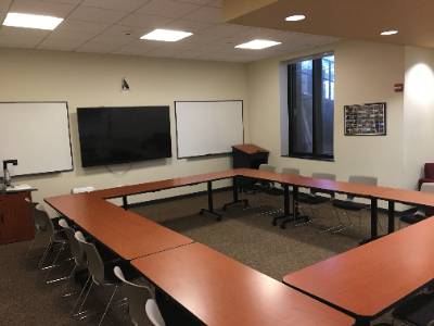Tables arranged in a rectangle, large television, 2 whiteboards