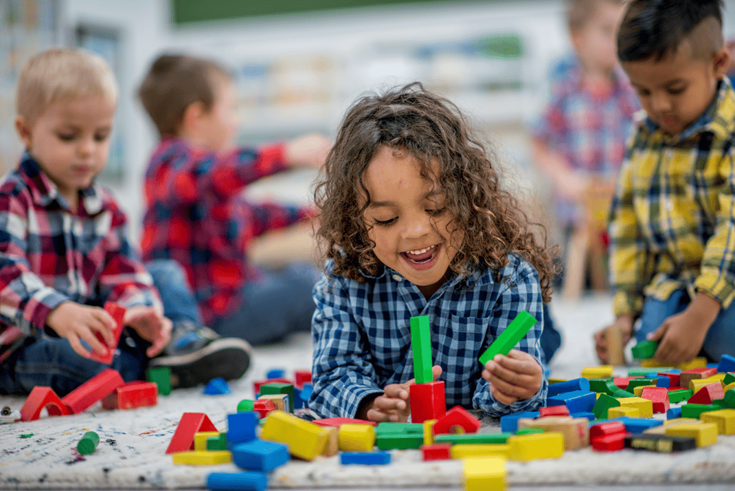 Child playing with building block toys on the floor with other children