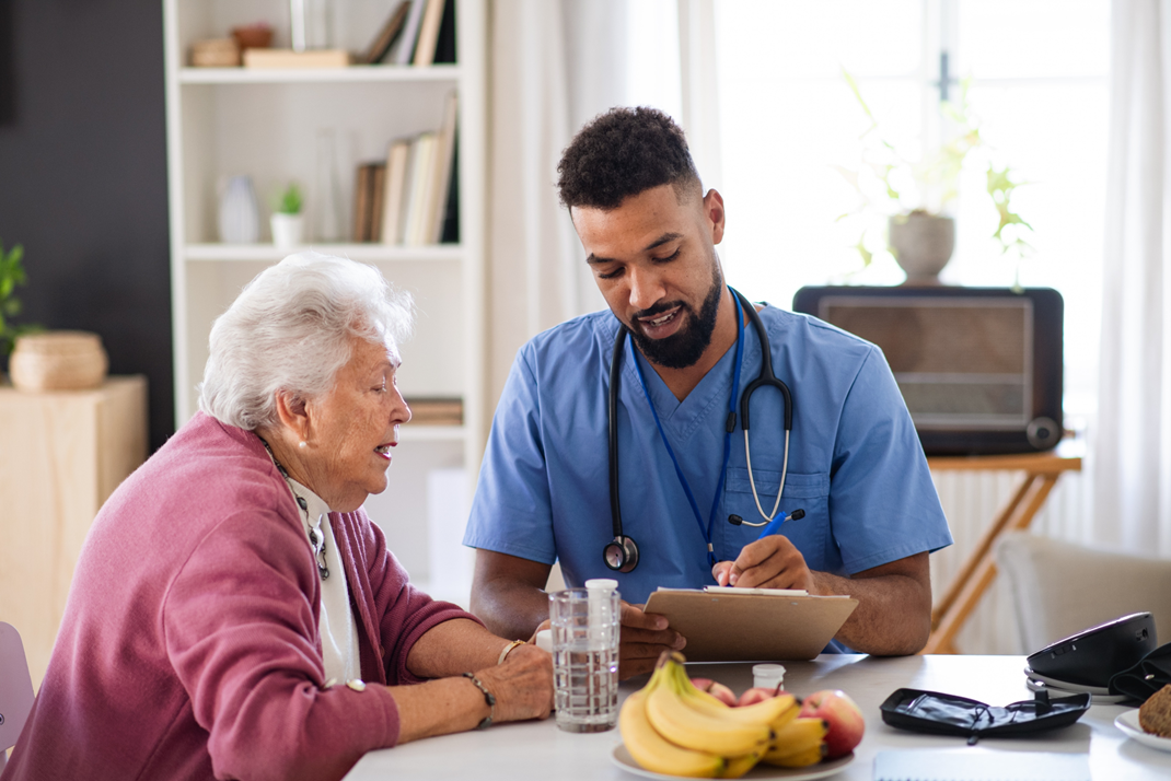 elderly woman sitting at table with a nurse going over a document on a clipboard