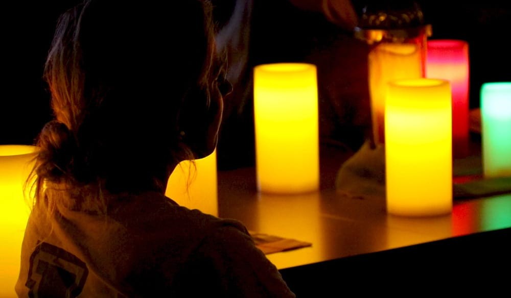 Side shot of a girl sitting in a dimly lit room surrounded by colorful candles