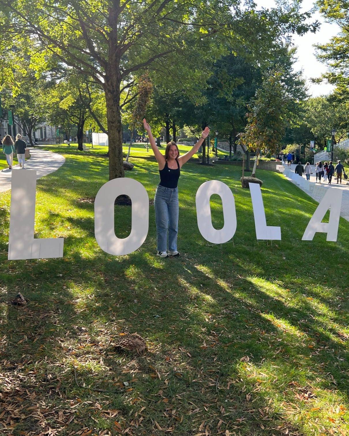 Student standing in between giant letters that spell LOYOLA, but the student replaces the Y by standing in its place with her arms raised