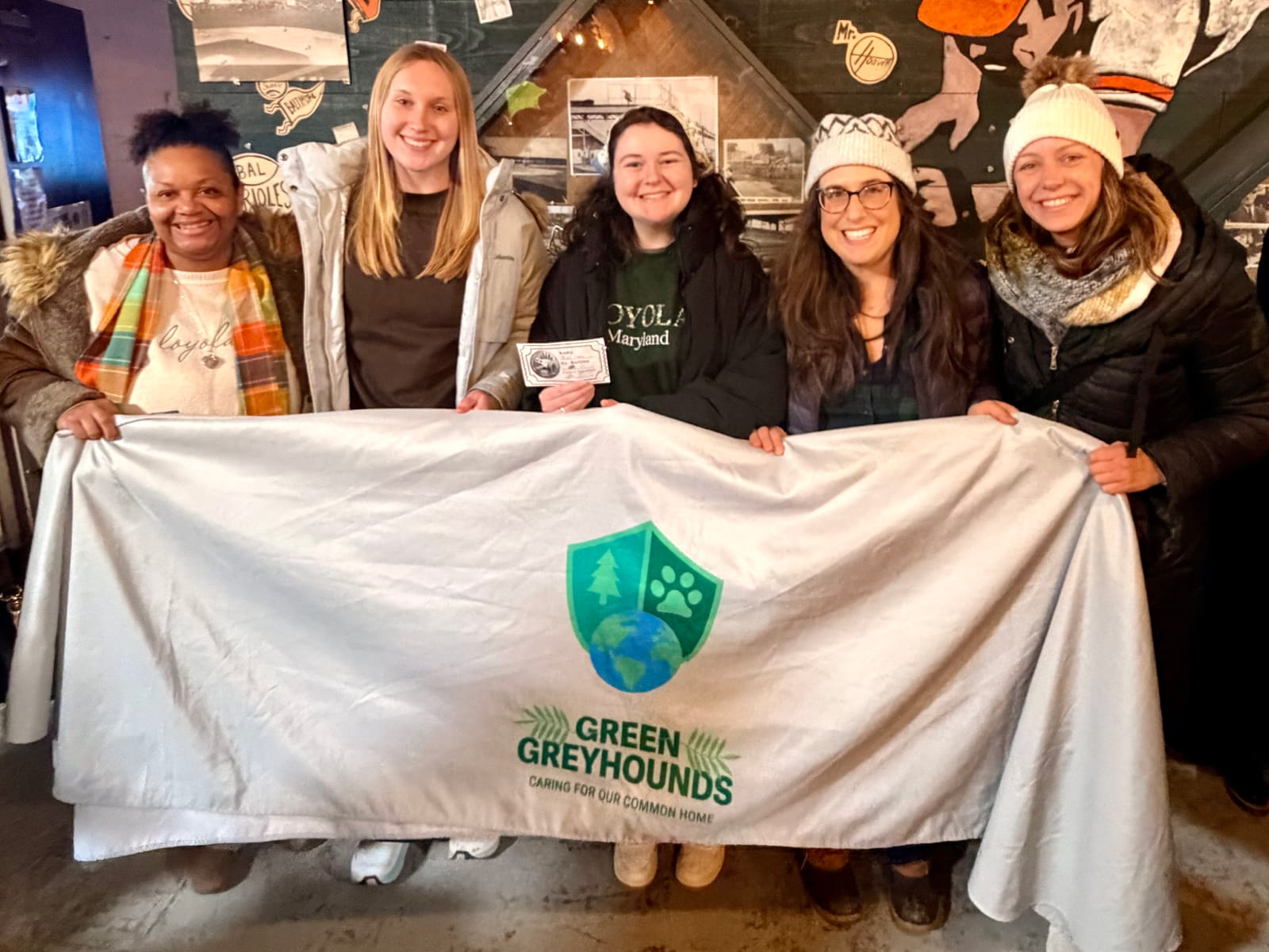 students holding up a banner reading green greyhounds and a shield shaped logo