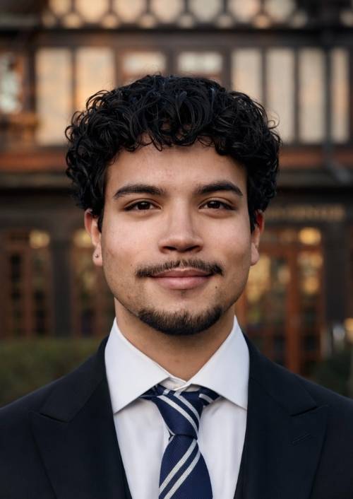 Juan standing with his arms crossed across his chest, smiling at the camera as he stands in front of the Humanities building.