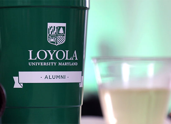 Green Loyola University Maryland Alumni branded reusable solo cup next to a glass of wine