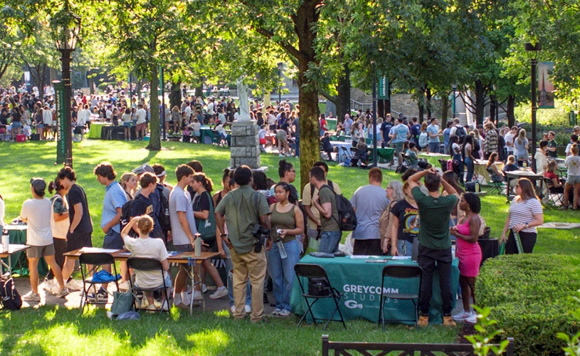 Large groups of students talking at information tables outside on the grassy quad during the activities fair