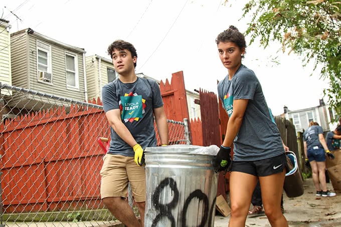 Students carrying garbage can in alley