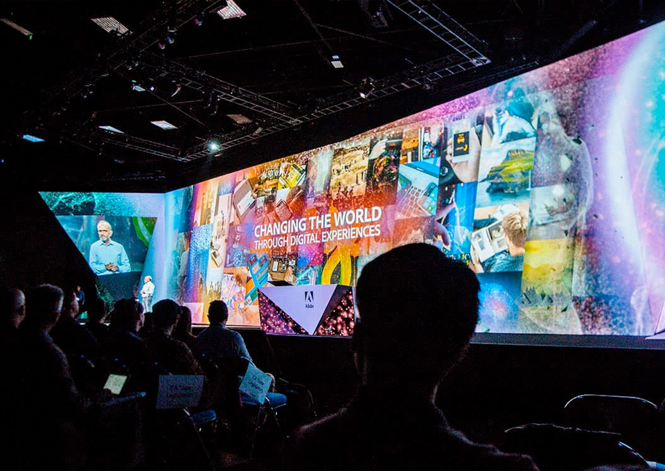 The stage at the Adobe Max conference. The backdrop is filled with lots of colorful images.