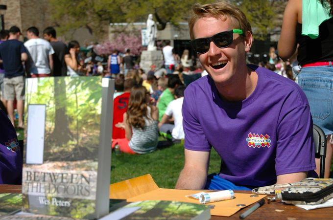 Student author Wes Peters, ’16 sits at a table marketing his book.