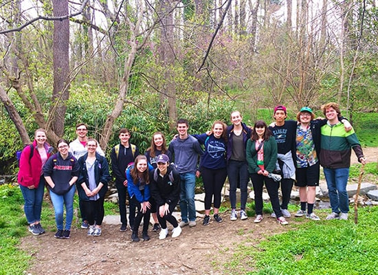 Honors students posing for a group photo on a wooded trail during a hike