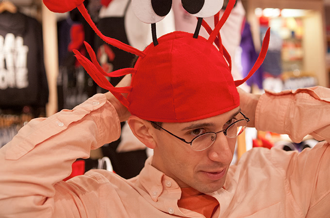 A student with glasses tries on a red crab hat