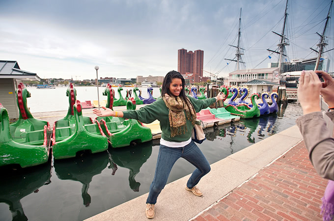 A student poses in front of dragon paddle-boats parked in the harbor