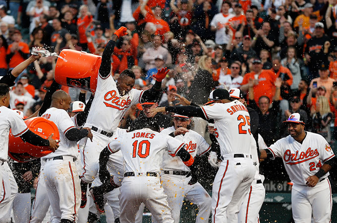 Baltimore Orioles baseball players celebrate at home plate in front of a cheering crowd