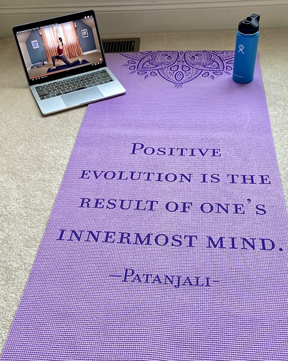 A laptop with a YouTube video of a yoga lesson sits by a yoga mat