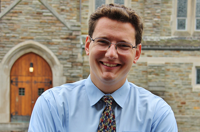 Krahel crosses his arms and smiles in front of Alumni chapel.