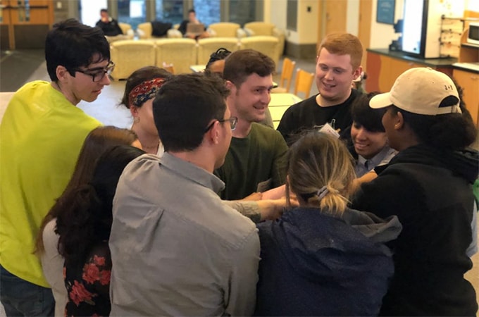 A group of students in the Social Impact Fellowship program huddle together to celebrate during a meeting