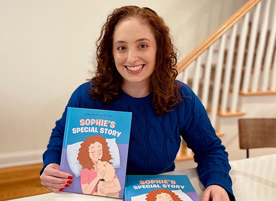Gabriella Gizzo holding up a copy of her book 'Sophie's Special Story' and posing for a photo